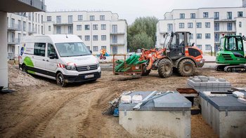 Auf der Baustelle stehen ein Lieferwagen und mehrere Baumaschinen, umgeben von neuen Wohngebäuden und Baustellenmaterial.