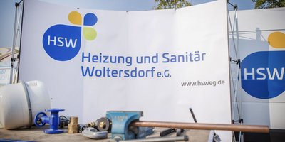Ein Werbebanner für HSW, das Heizungs- und Sanitärdienstleistungen in Woltersdorf anbietet, steht vor einer Werkstatt.