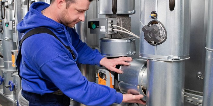 Ein Techniker in blauer Arbeitskleidung arbeitet an einer silbernen Rohrleitung und überprüft die Verbindung.